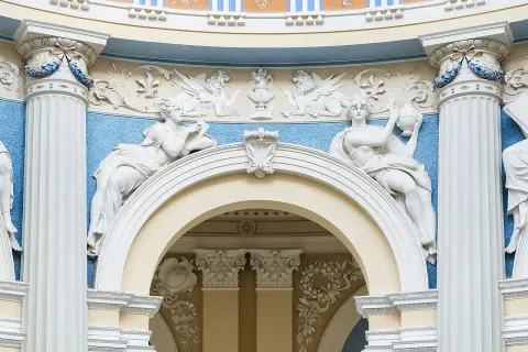 Barokowe stiuki: rzeźby kobiet, gryfy i ornamenty na tle błękitnej ściany.