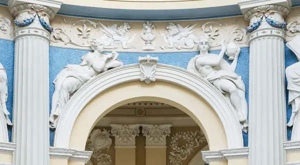 Barokowe stiuki: rzeźby kobiet, gryfy i ornamenty na tle błękitnej ściany.
